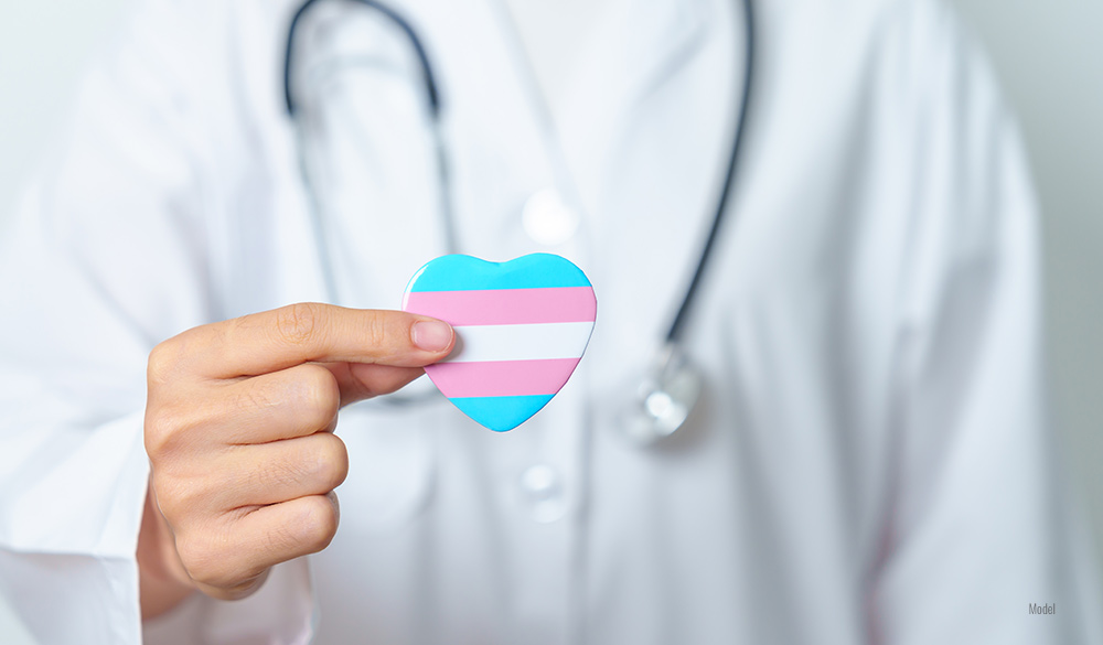 A doctor with a stethoscope holds up a heart with the transgender flag colors